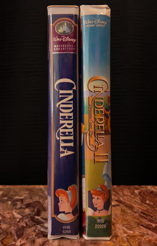 Two VHS tapes of 'Cinderella' and 'Cinderella II' from the Walt Disney Home Video collection on a wooden surface with a dark background.